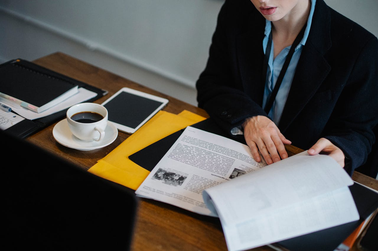 Businesswoman analyzing documents with coffee at a desk using a tablet. Professional workspace setting.