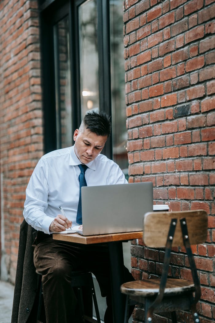 Professional man working on a laptop at an outdoor cafe table, focused on remote tasks.